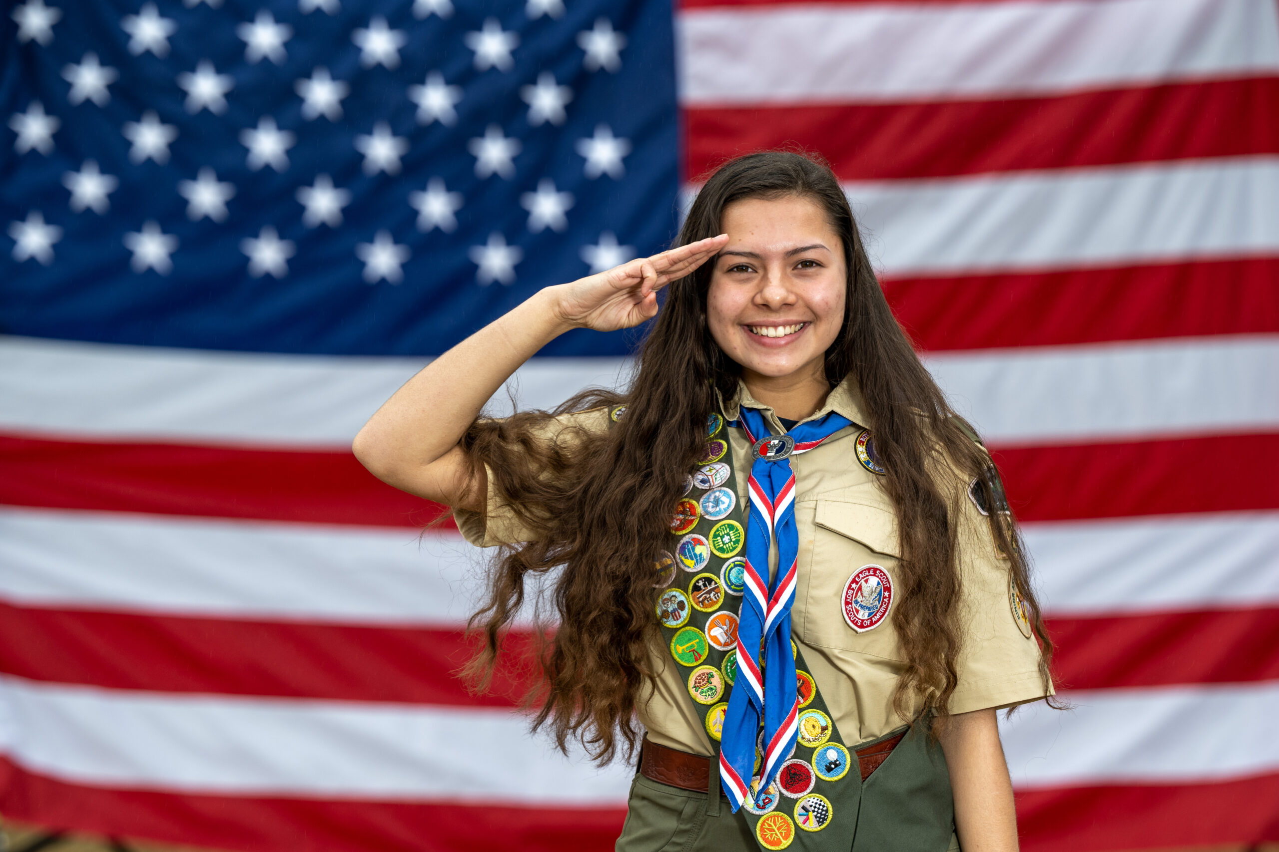 Eagle scout wearing a merit badge sash saluting in front of an American flag